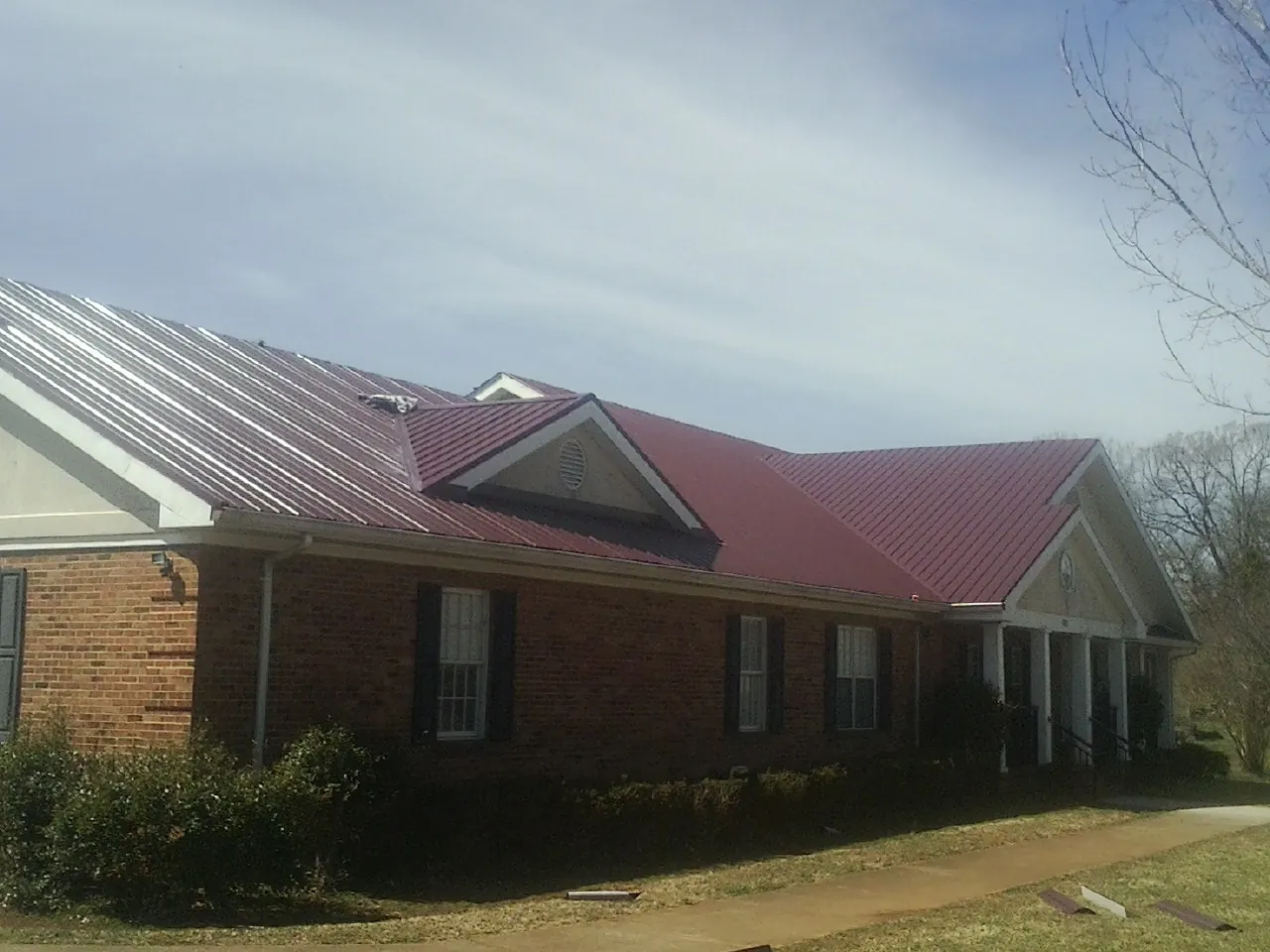 Red metal roof with gabled entries on a long brick building, from a Hail Damage Roof Repair job in Turkey