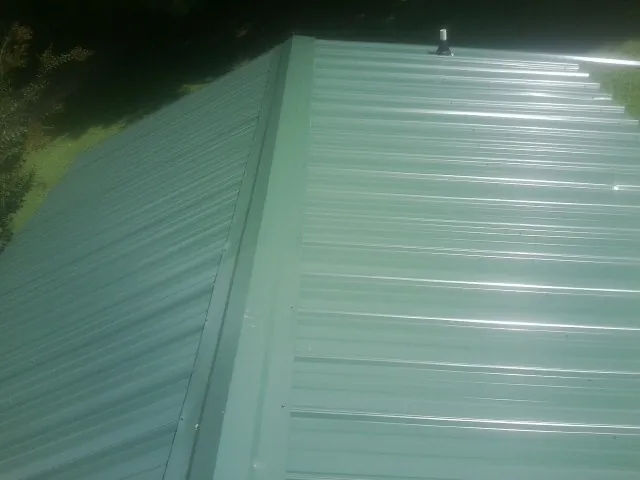 New green metal panels meeting at the ridge of a roof — Flat Roof Repair work by our crew in Turkey